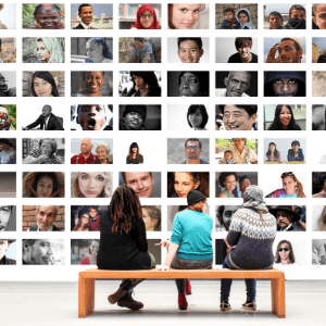 museum wall with photos, three people sit on bench in front